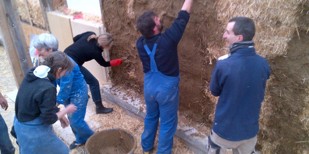 Plusieurs personnes appliquent un enduit sur un mur en bottes de paille lors d’un atelier pratique.