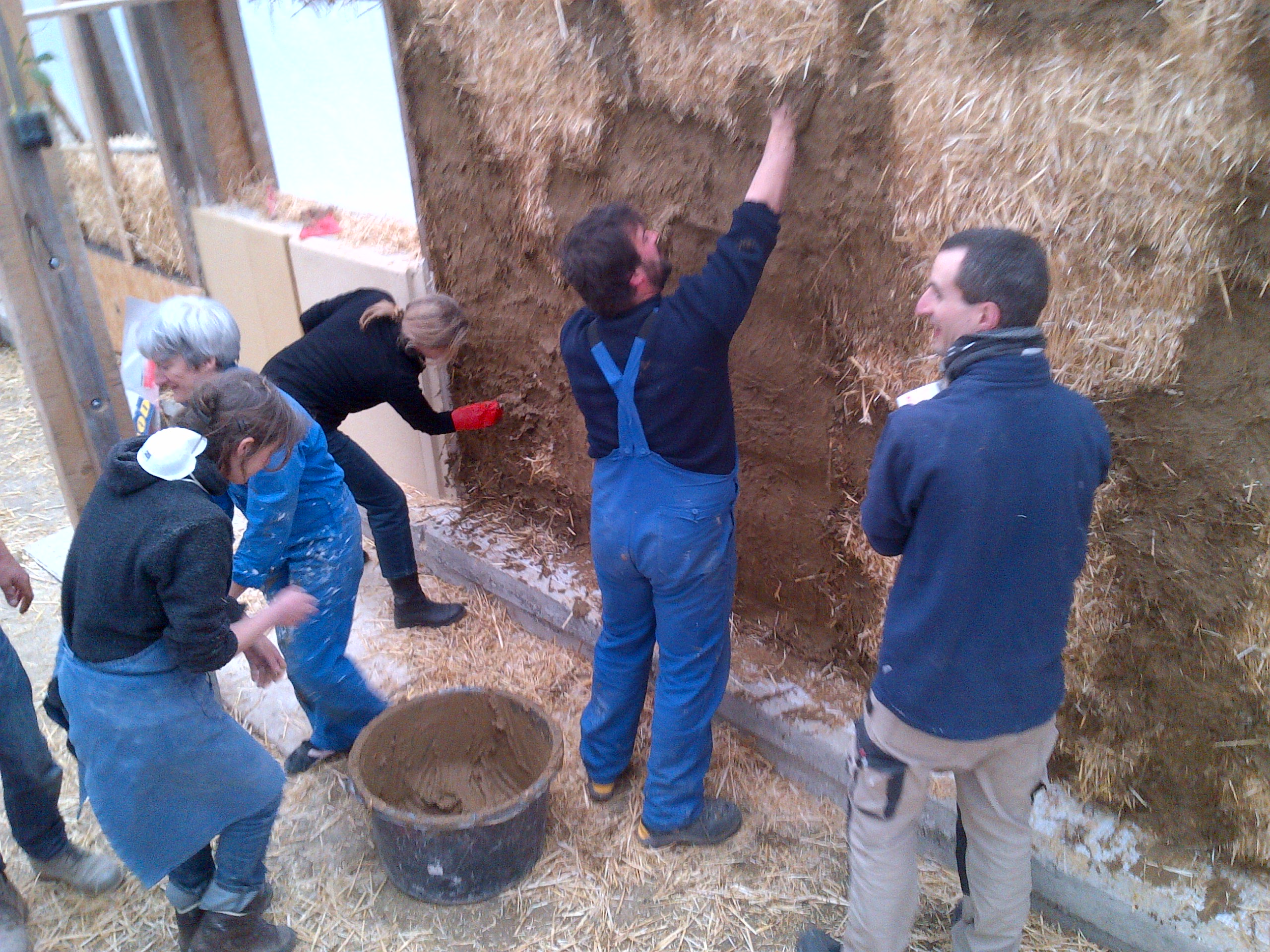 Plusieurs personnes appliquent un enduit sur un mur en bottes de paille lors d’un atelier pratique.