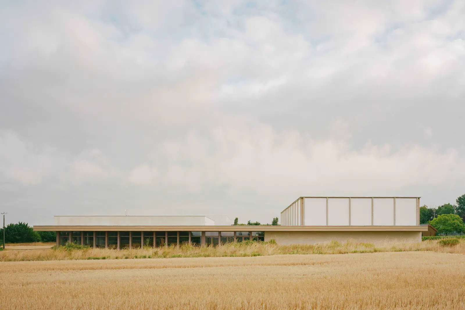 Le complexe sportif de Parçay-Meslay vu depuis un champ, avec une longue façade basse et deux volumes plus hauts.